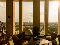 Terrasse mit Sitzgruppen aus Sesseln und Tischen vor großen Säulen mit Blick auf die Stadt Nürnberg bei Sonnenlicht