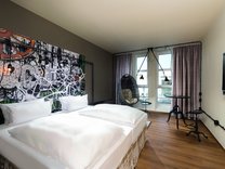 Modern eingerichtetes Hotelzimmer mit zwei Einzelbetten, großem Fenster, Flachbildfernseher an der Wand und floral gemusterter Wanddekoration
