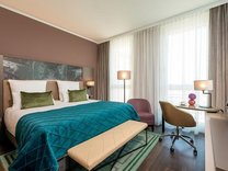 Modern eingerichtetes Hotelzimmer mit Doppelbett, Sitzbank, Schreibtisch und großem Fenster mit Vorhängen