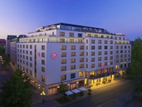 Großes mehrstöckiges Hotelgebäude mit beleuchtetem Eingangsbereich und Sheraton-Logo an der Fassade bei Dämmerung