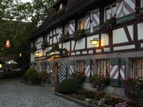 Fachwerkfassade des Romantik Hotel Gasthaus Rottner mit beleuchteten Fenstern und Blumenschmuck am Abend.