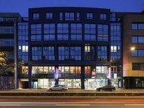 Fassade des Ibis Hotels am Hauptbahnhof Nürnberg bei Abenddämmerung mit beleuchteten Fenstern und zwei parkenden Autos davor